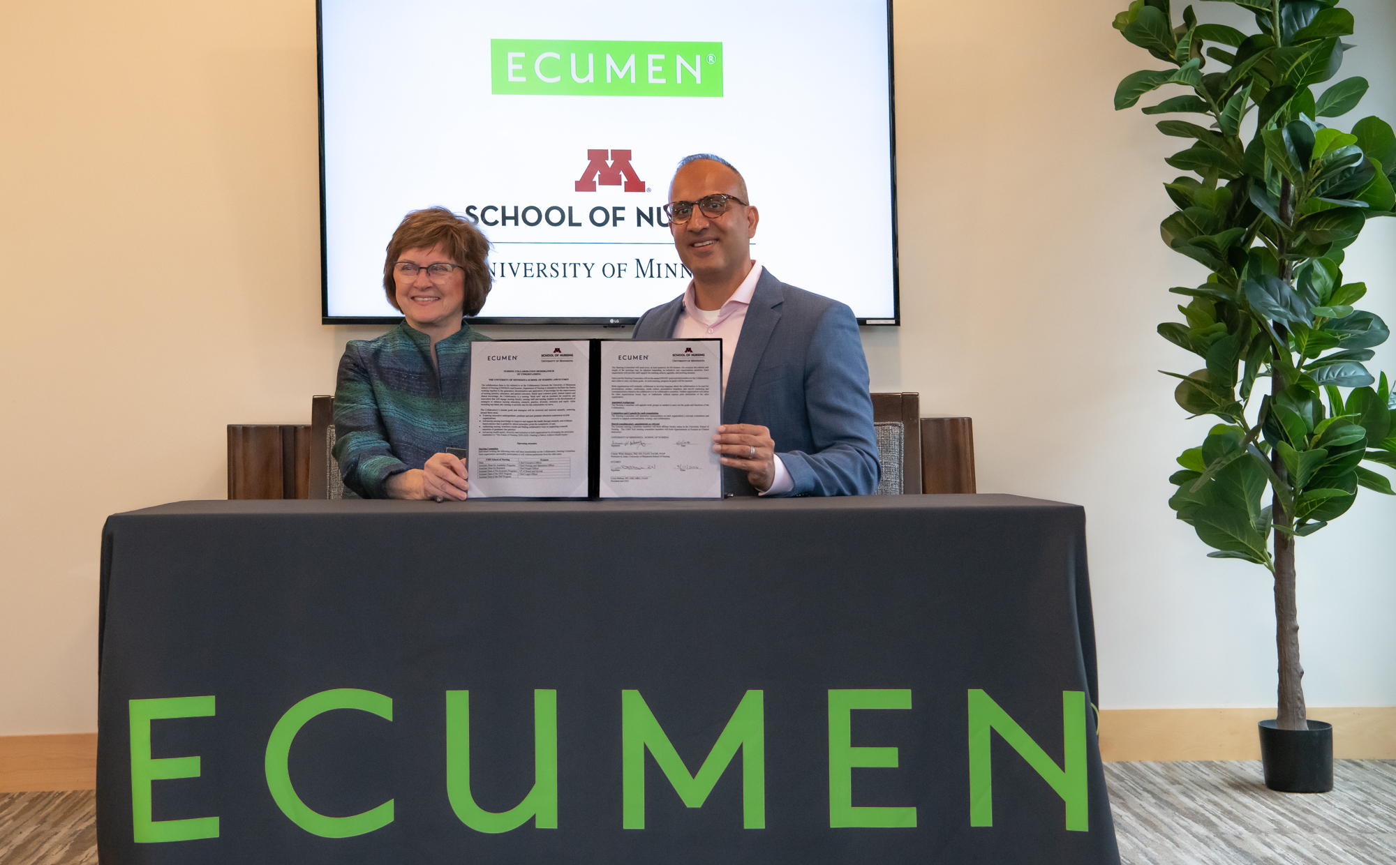 Ecumen President & CEO Cryus Batheja and Dean Connie White Delaney holding up signed doc commemorating the partnership between Ecumen and the U of M School of Nursing