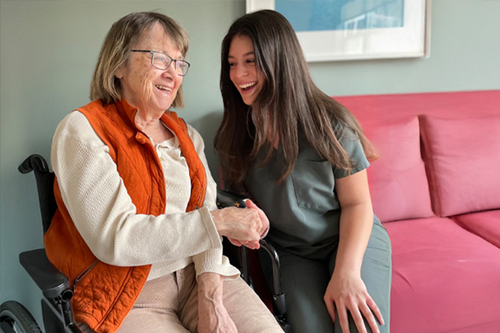 Smiling older woman in a wheelchair shaking hands with a happy caregiver in a living room.