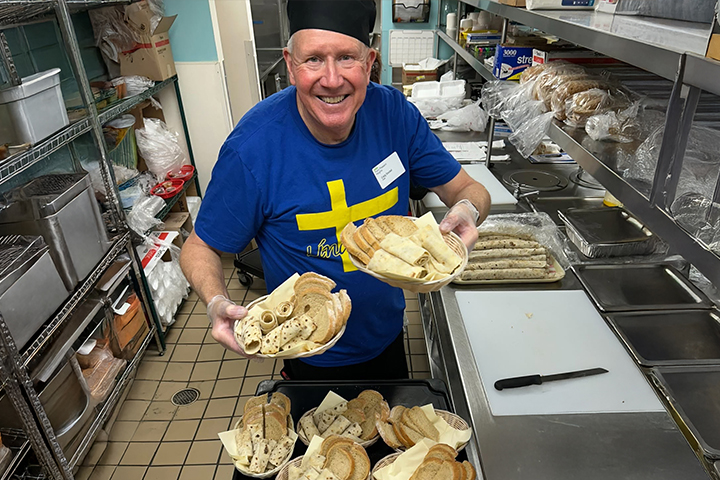 An older man in a commercial kitchen smiles as he prepares baskets of bread and lefse, a traditional Scandinavian flatbread..