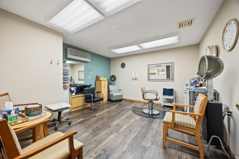 Interior salon with upholstered arm chairs, shampoo sink, styling chair, and two hair drying stations.