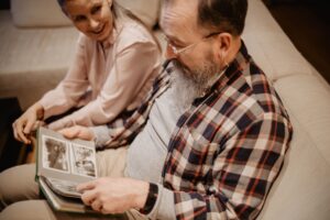 An older couple reminiscing with a photo album on a comfortable sofa indoors.